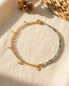 Gold bracelet with green beads on a beige fabric background