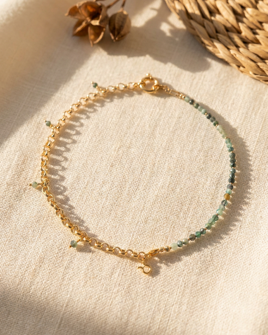 Gold bracelet with green beads on a beige fabric background
