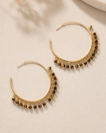 Gold hoop earrings with brown beads on a beige surface with dried flowers.